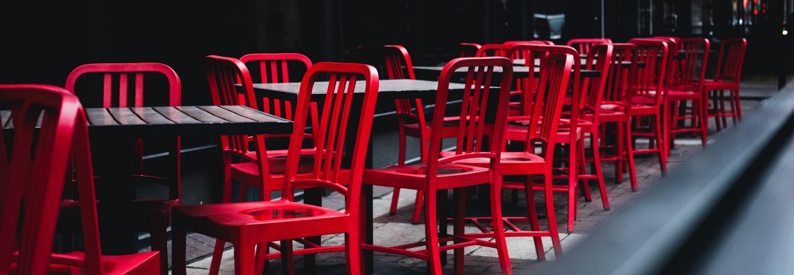 Leere rote Stühle draussen vor einem Restaurant.