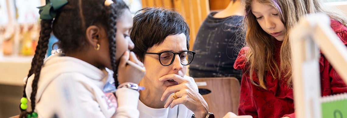 Susanne Hartmann arbeitet mit zwei Kindern an einer Aufgabe in der Schule